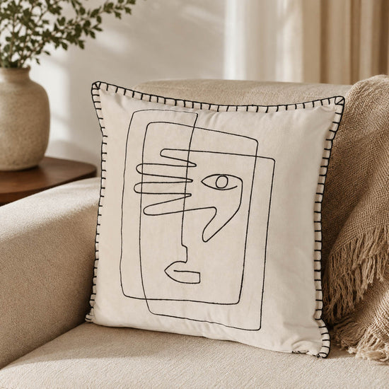 Cremeweißes Kissen mit Gesicht auf einem Sessel im Boho-Look