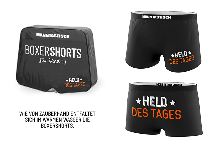 Magische Boxershorts „Held des Tages“ – schwarze Fun-Shorts mit weiß-orangefarbenem Spruch & MANNTASTISCH-Bund von Geschenk für Dich, Männergeschenk
