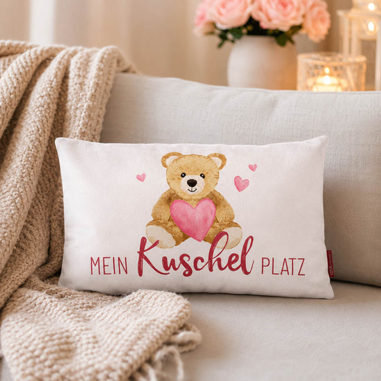 Kissen mit Spruch Mein Kuschelplatz, Teddy mit Herz, rote Rückseite, auf Holz mit Geschenk und Lichterkette