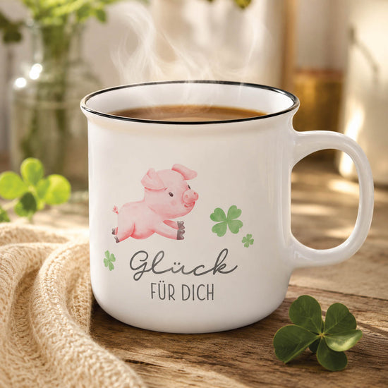 Kultbecher „Glück für Dich“ in Weiß mit Glücksschweinchen, stimmungsvoll auf Holztisch mit vierblättrigen Kleeblättern und Strickdecke – Geschenk für Dich